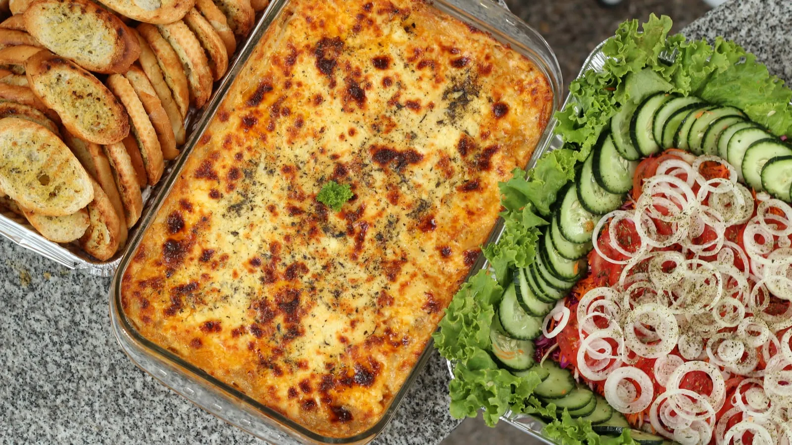 Bandejas de lasaña con ensalada y pan de ajo para catering de Tamarinda en Quito